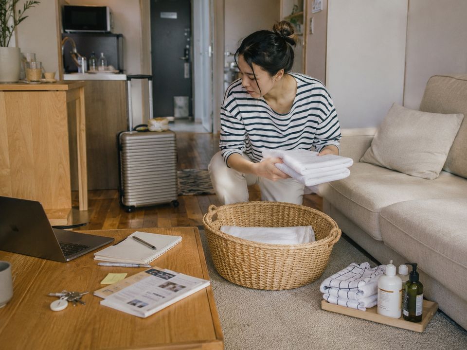 Owner folding fresh towels beside a laundry basket in her furnished apartment